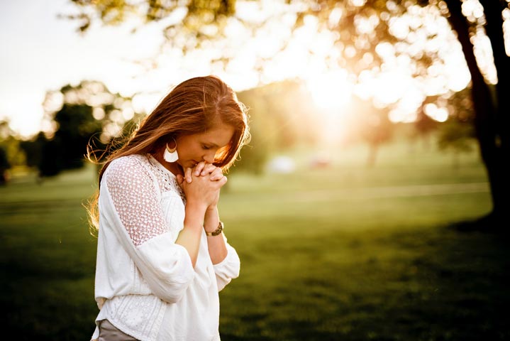 Ung kvinna utomhus i solnedgång, knyter sina händer och ber